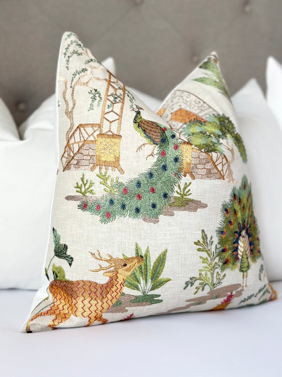 Chinoiserie-style designer throw pillow cover featuring embroidered deer and peacock motifs in orange and green on a white linen background. Chinoiserie pillow, designer throw pillow, embroidered pillow, deer peacock motif, orange embroidery, green embroidery, luxury pillow cover