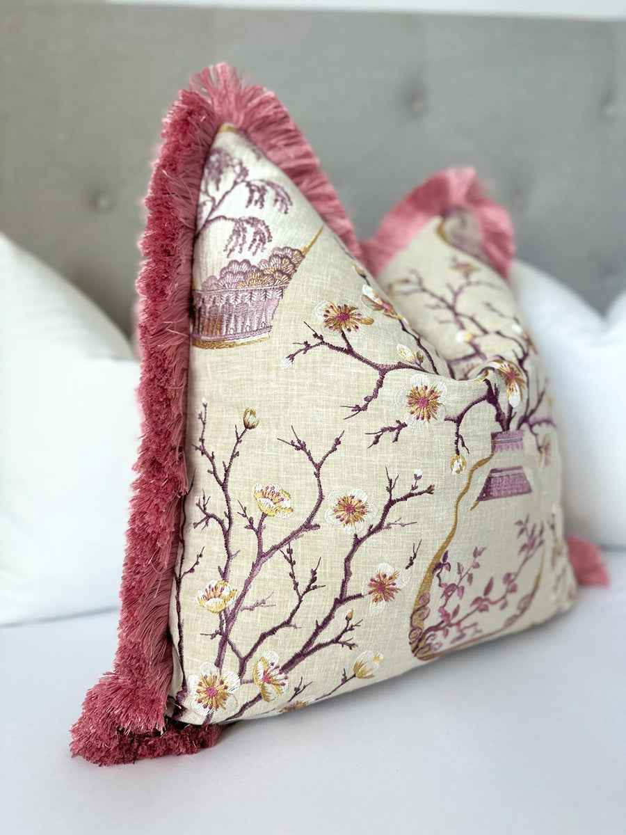 Chinoiserie pillow cover with pink floral embroidery, orange accents, a beige linen base, and pink fringe; a luxurious blend of elegance and modern design for sofas or bedrooms.